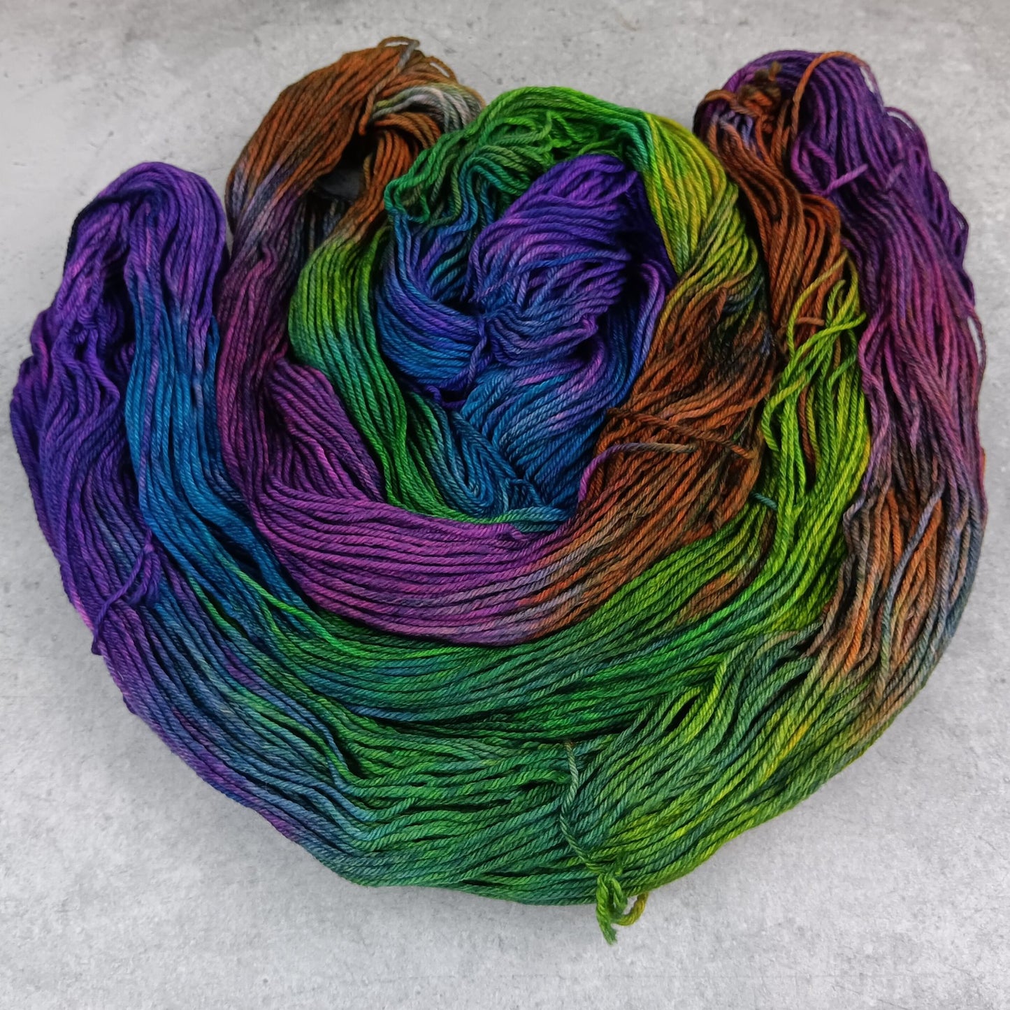 Two skeins of multicolored yarn in a moody rainbow variegated colourway on a gray surface