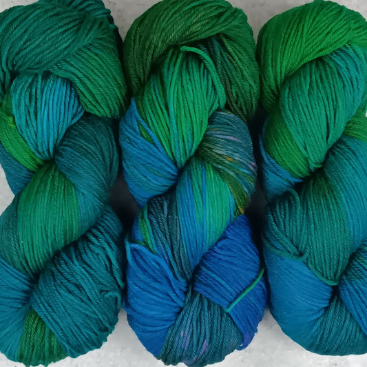 Three skeins of multicolored yarn in a variegated colourway with deep greens, blues, and little of purple on a gray surface