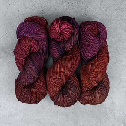 Three skeins of maroon and purple yarn on a gray surface