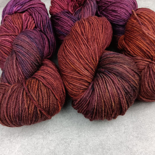 Two skeins of multicolored yarn in a maroon and purple variegated colourway on a gray surface