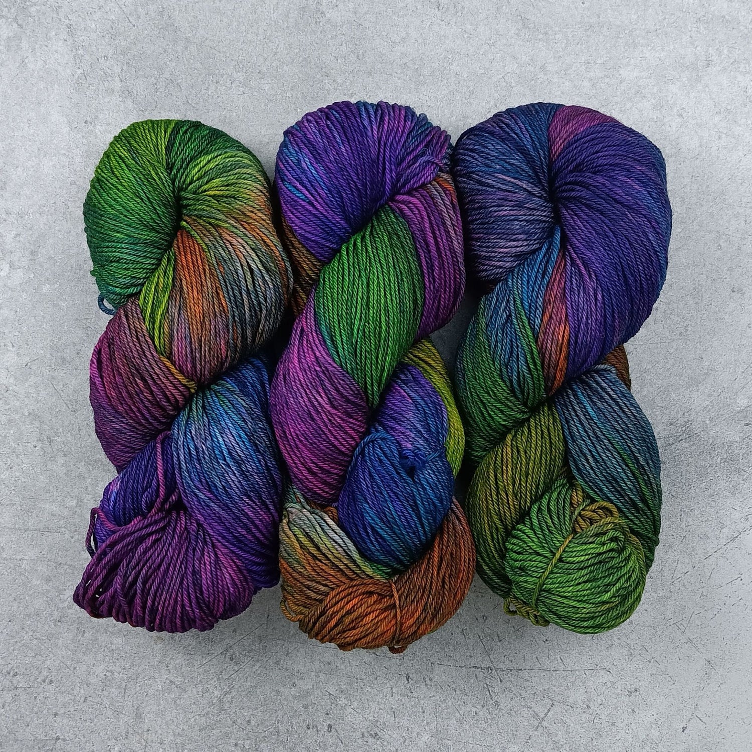 Three skeins of multicolored yarn in a moody rainbow variegated colourway on a gray surface