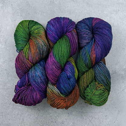 Three skeins of multicolored yarn in a moody rainbow variegated colourway on a gray surface