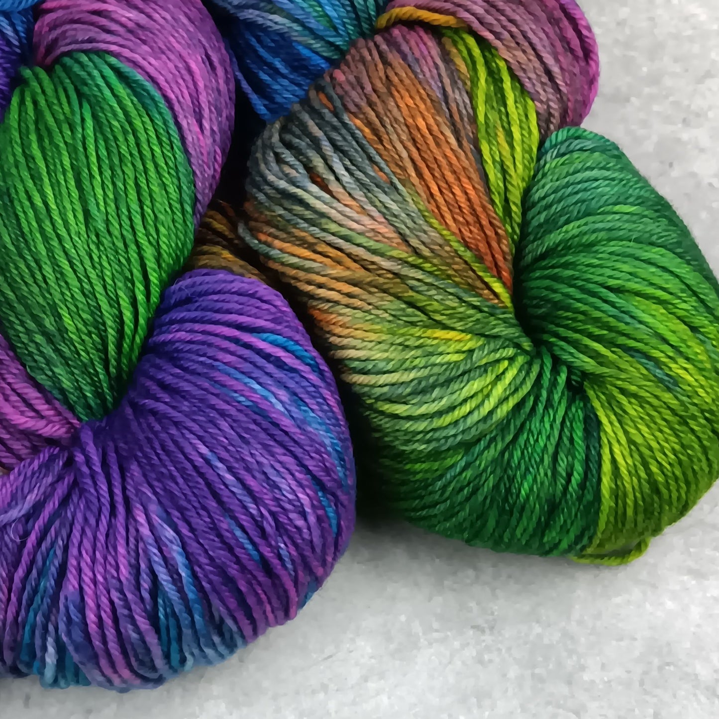 Two skeins of multicolored yarn in a moody rainbow variegated colourway on a gray surface