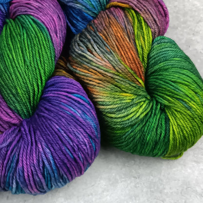 Two skeins of multicolored yarn in a moody rainbow variegated colourway on a gray surface