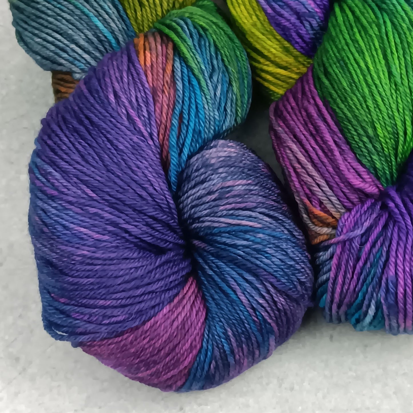 Two skeins of multicolored yarn in a moody rainbow variegated colourway on a gray surface