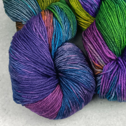 Two skeins of multicolored yarn in a moody rainbow variegated colourway on a gray surface